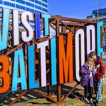 Two children pose in front of a sign that says Visit Baltimore