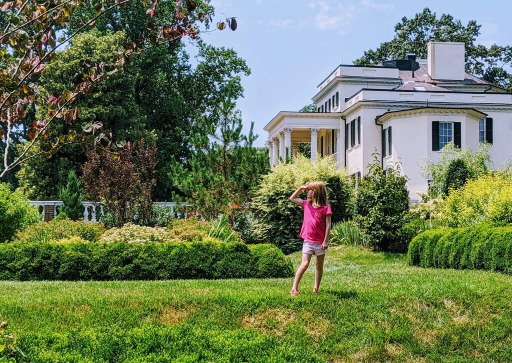 A girl shades her eyes as she looks out over the gardens in front of a plantation house at Oatlands Plantation in rural Virginia